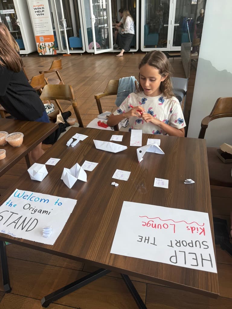 A girl running an origami stand she set up herself, with handmade signs and paper animals priced for sale