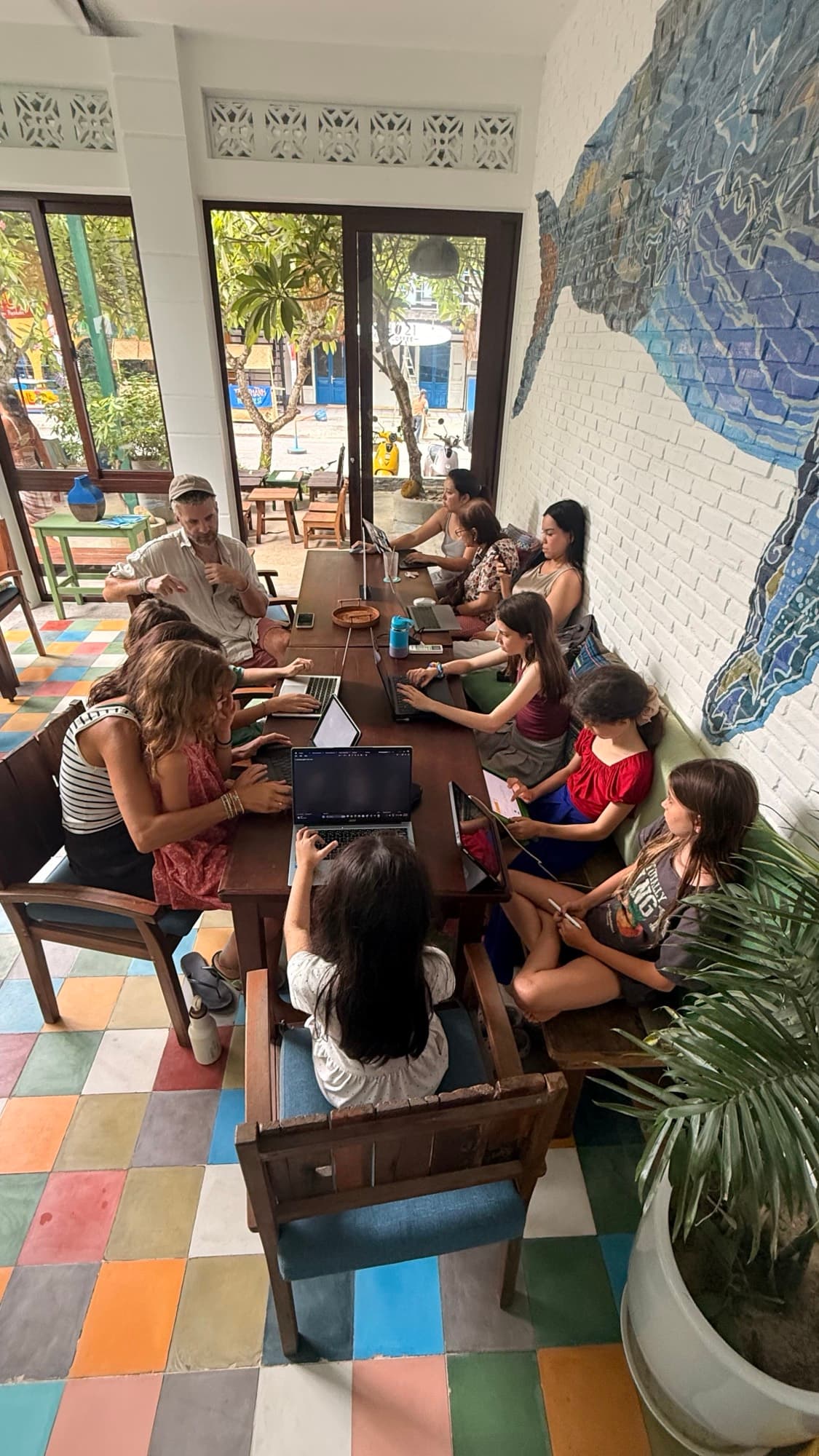 Parents and children working on laptops together around a long table in a Hoi An cafe