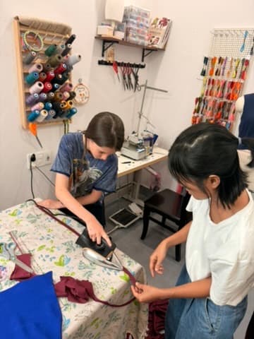 A child ironing fabric in a Hoi An tailor's studio, guided by a local maker