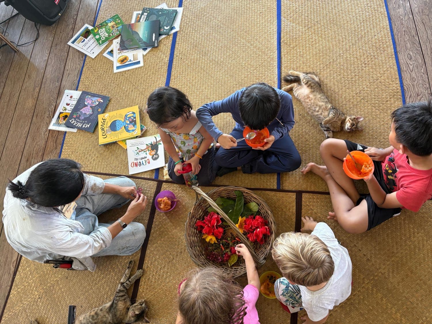 Children sharing books and bowls of fruit in a story circle on woven mats at Network School