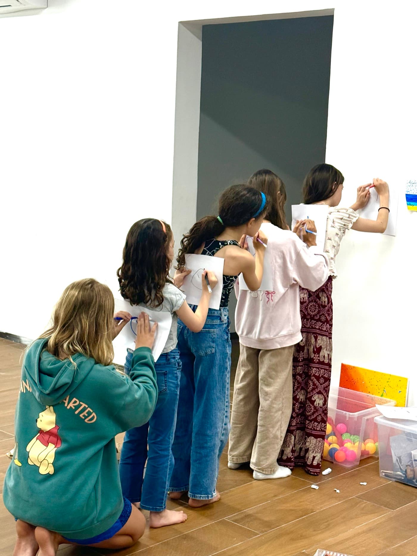 Five children sketching ideas on papers pinned along a wall