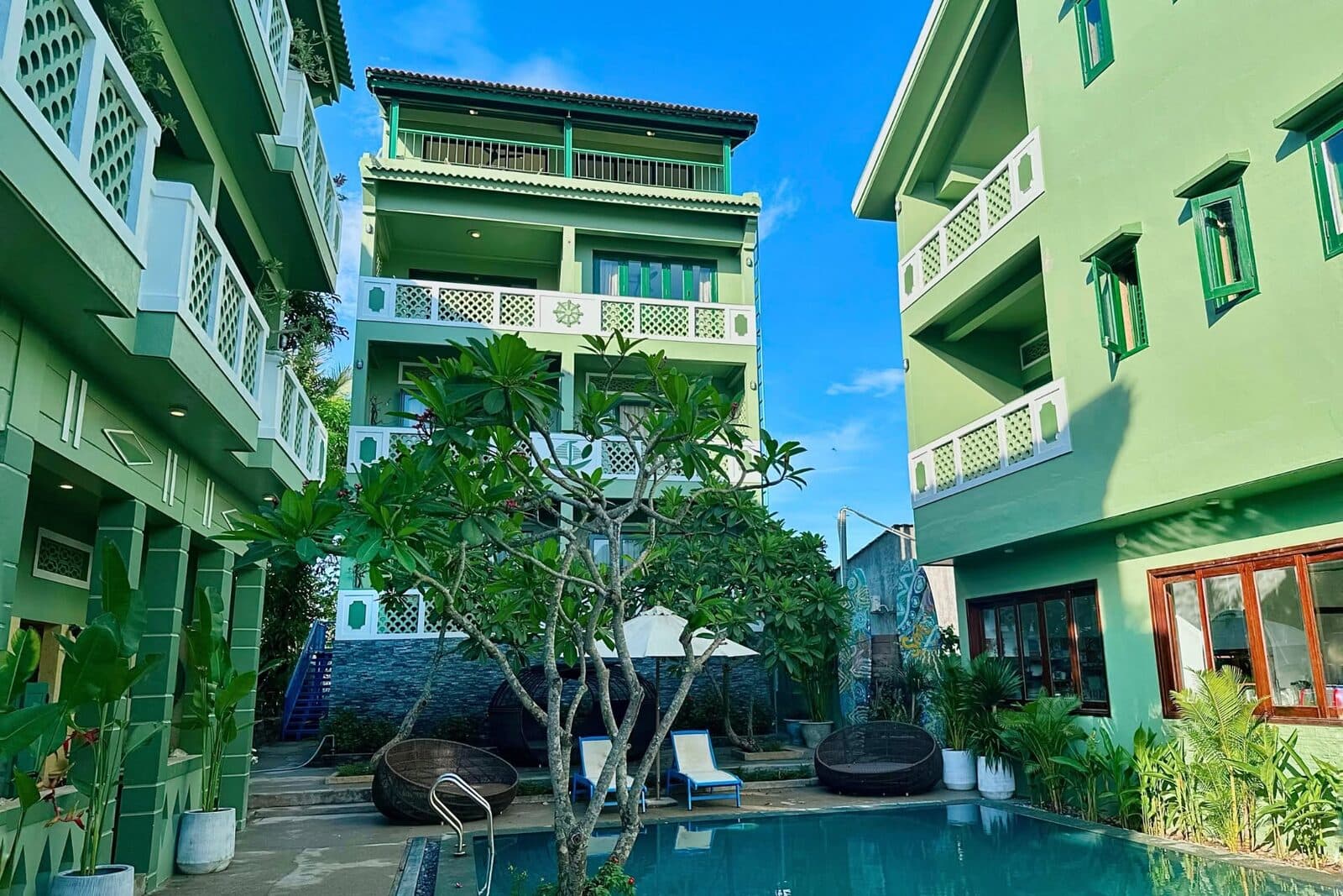 A swimming pool ringed by loungers and palms in the green courtyard of the collective