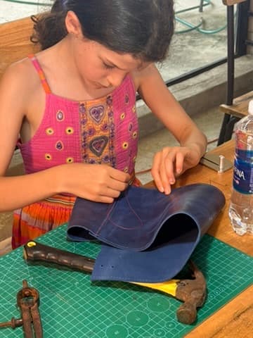 A girl working a piece of leather with focused attention at a workshop bench