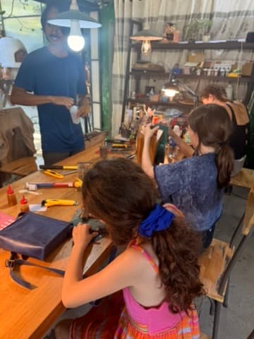 Children learning leather-craft from a workshop instructor at his bench in Hoi An