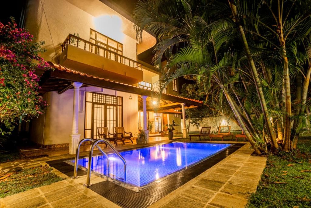 A villa pool lit blue at night, ringed by palms, bougainvillea, and a stone terrace