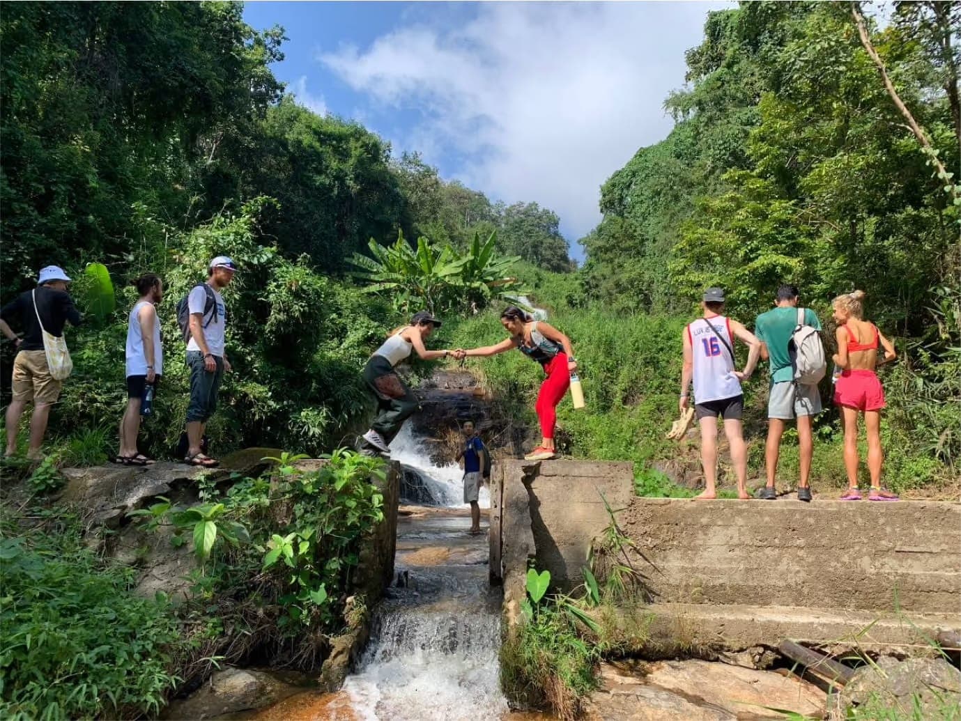 A group from a prior Edge City village crossing a jungle waterfall together on a weekend adventure