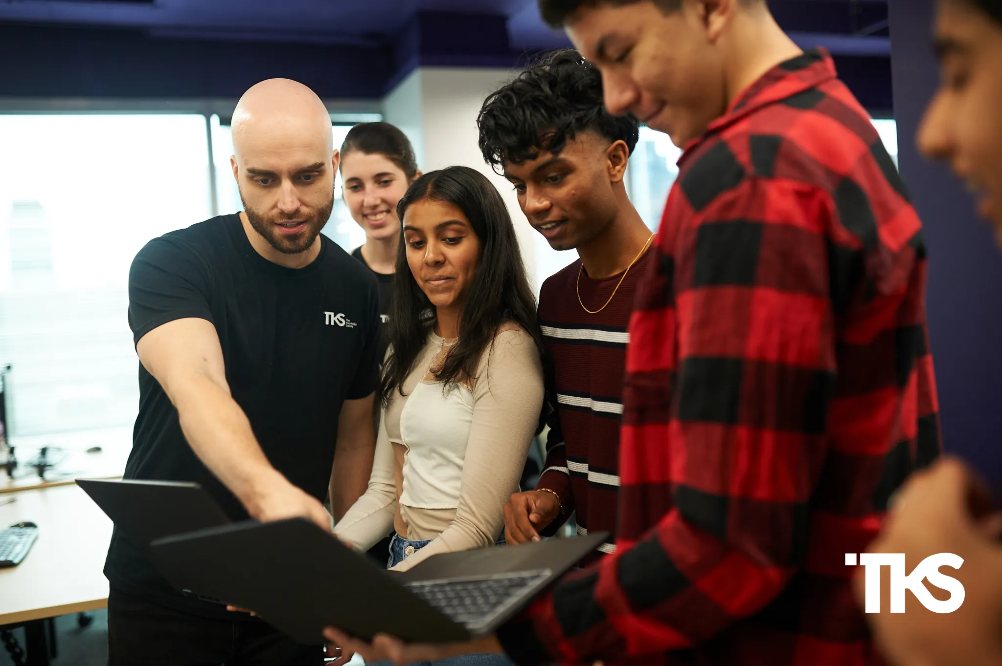 A TKS director mentoring five students gathered around a laptop